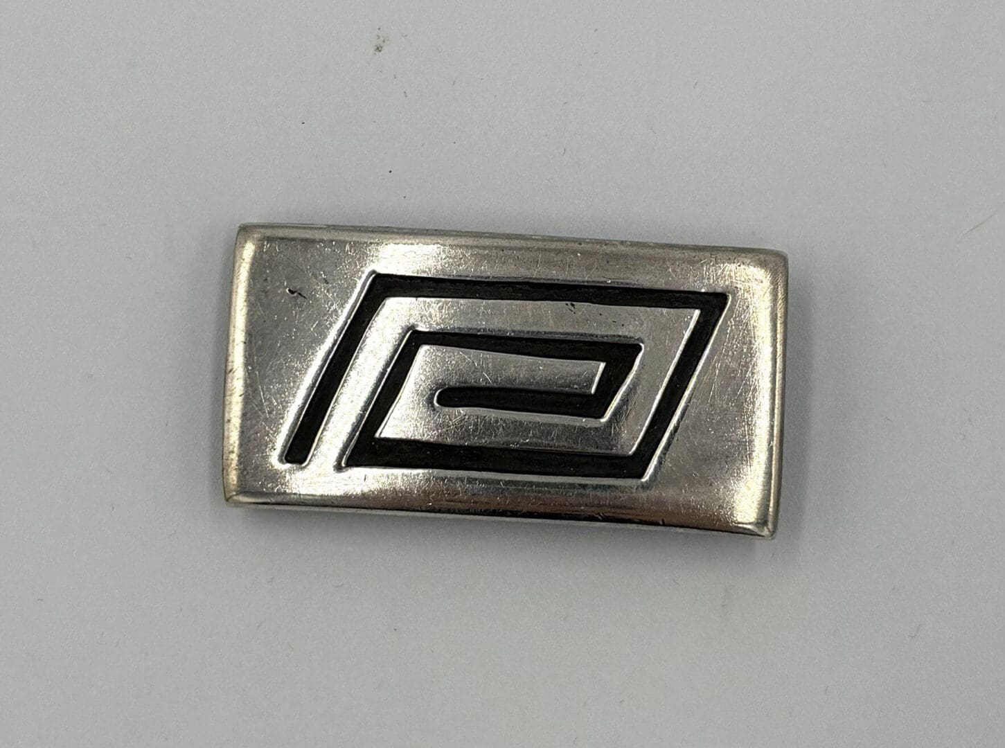 Rectangular silver pin with geometric design.