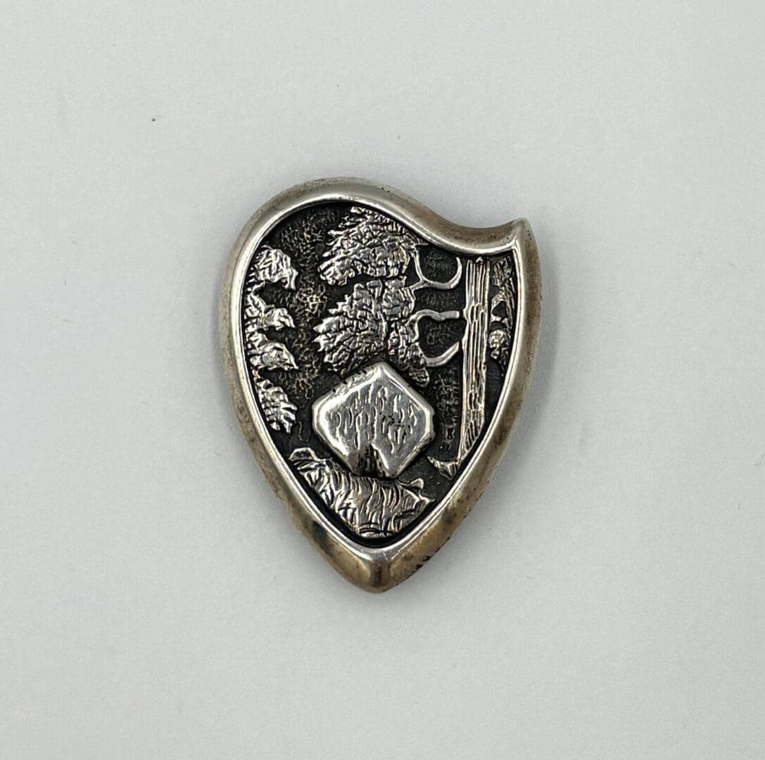 Shield-shaped pin with tree and mountain design.
