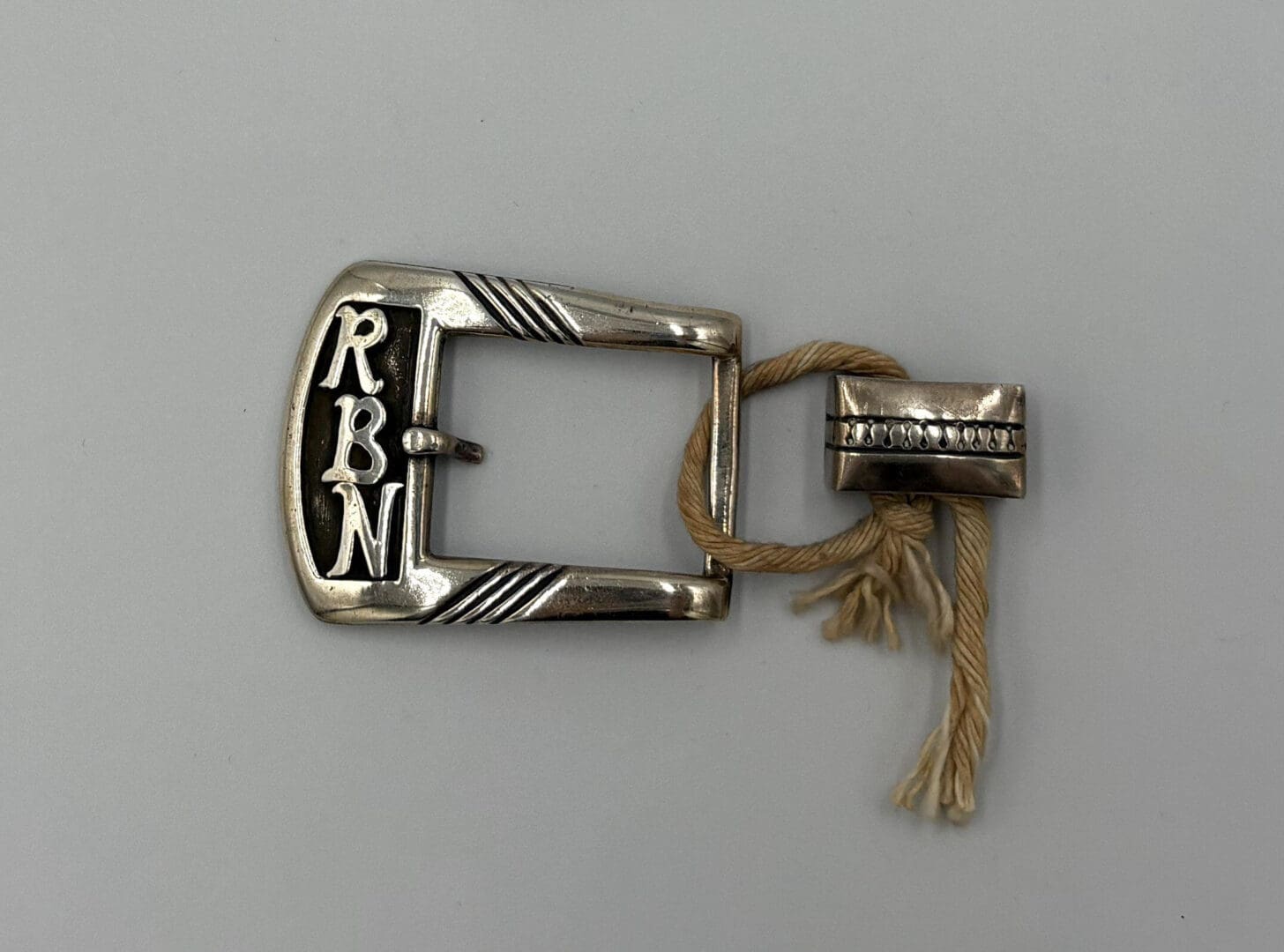 Silver belt buckle with initials and tag.