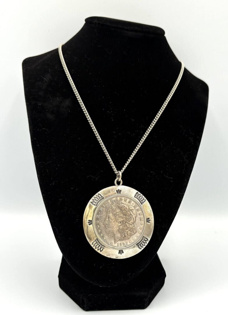Silver pendant necklace on black display stand.