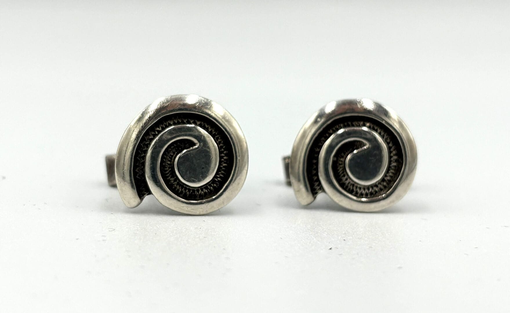 Silver spiral cufflinks on white background.