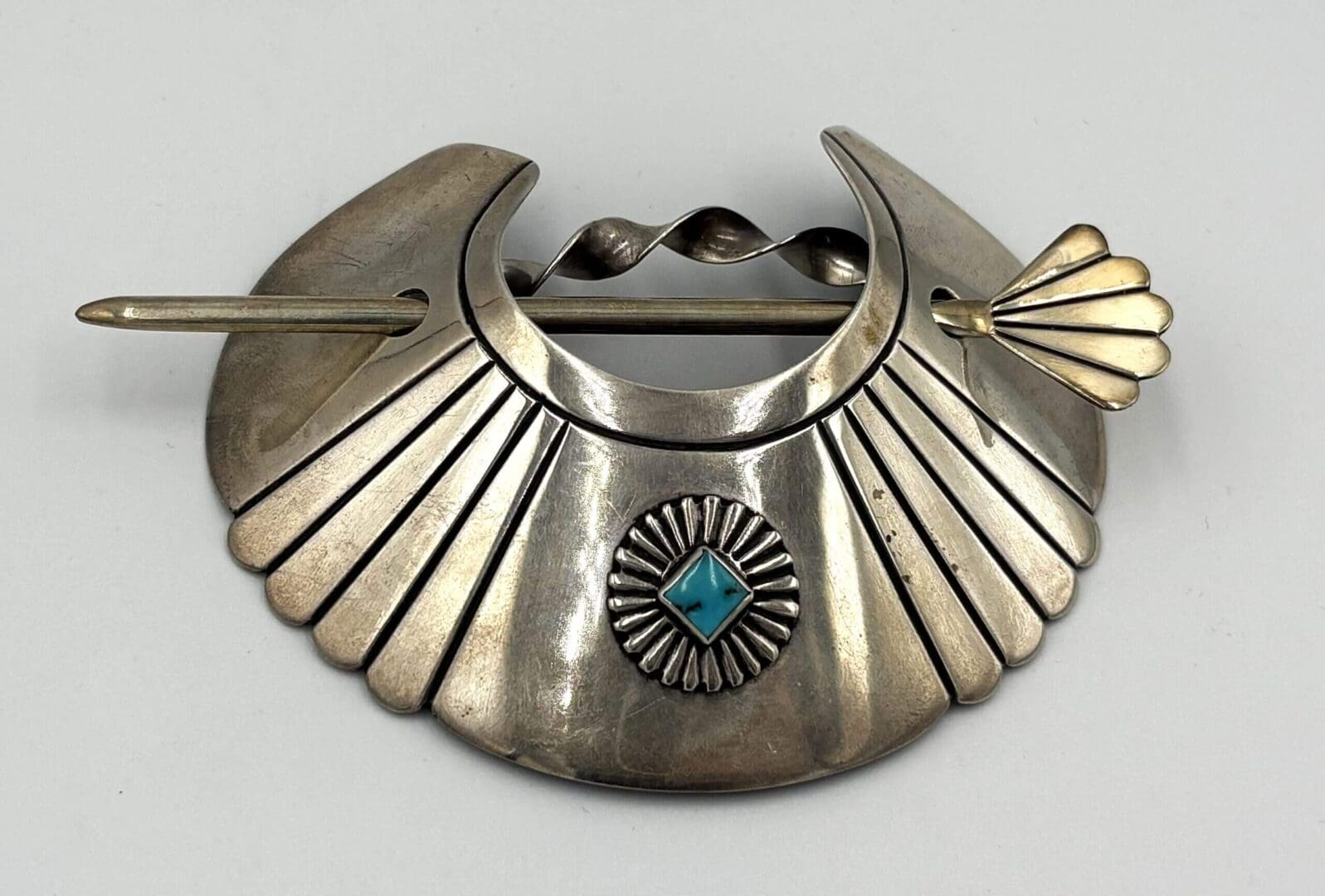 Silver brooch with turquoise and fan design.