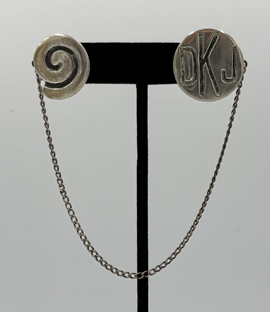 Silver cufflinks with chain on display stand.
