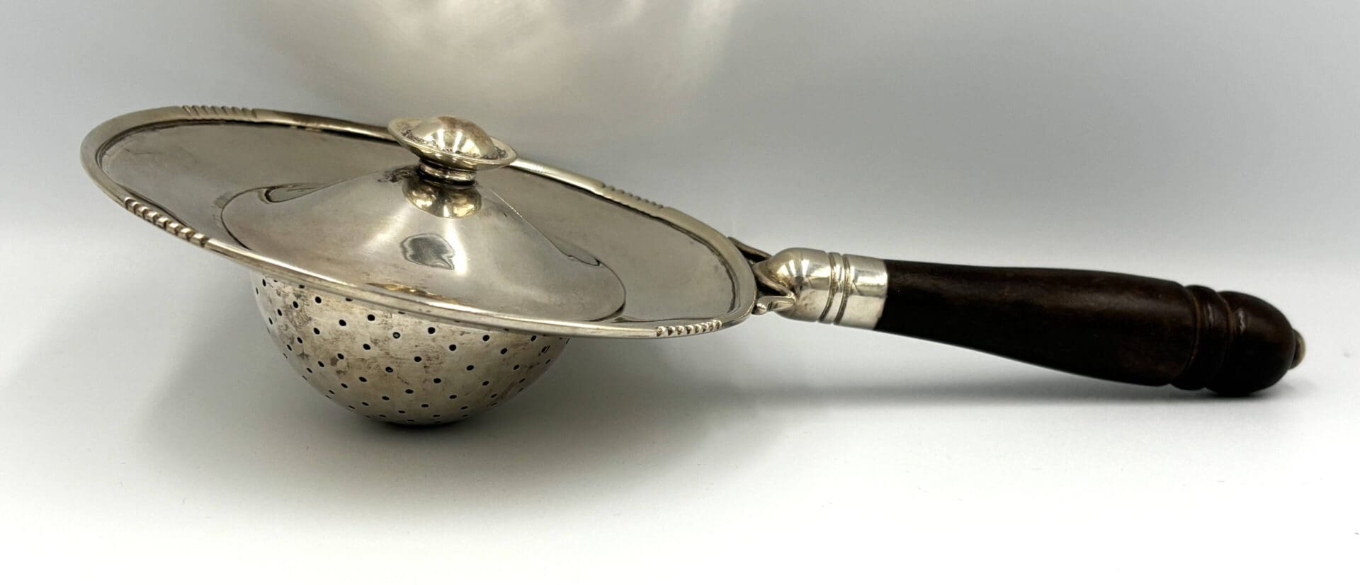 Silver tea strainer with dark wooden handle.