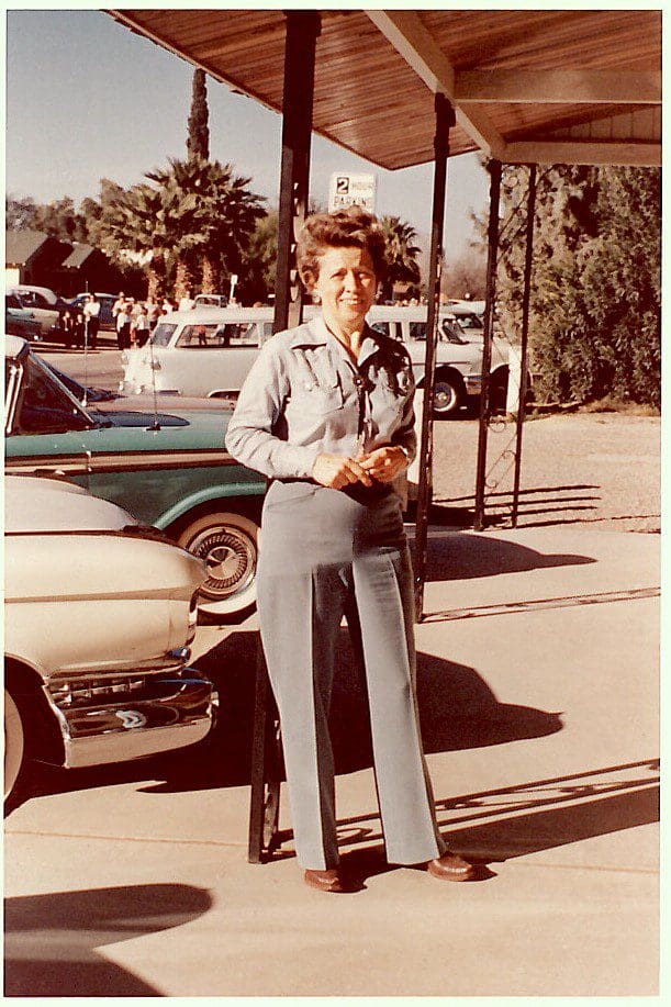 Woman standing outside near vintage cars.