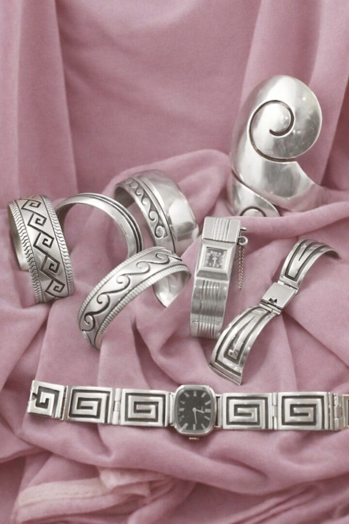 Silver jewelry displayed on pink fabric background.
