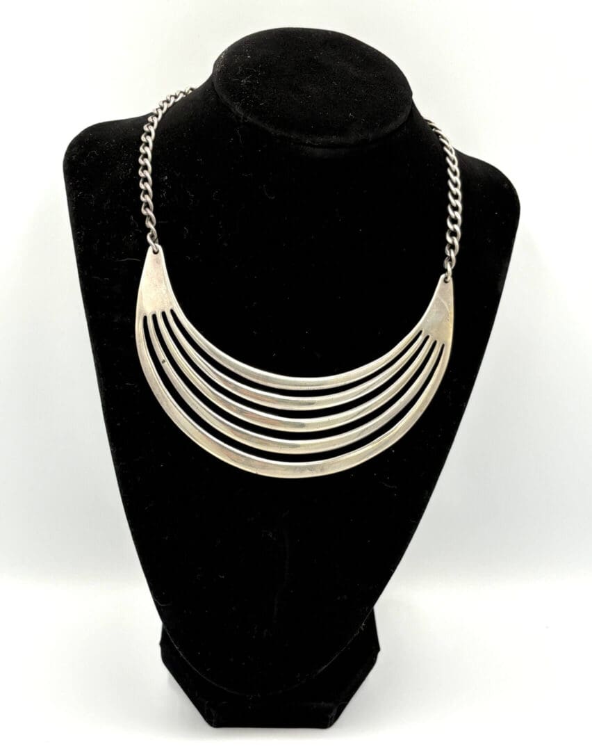 Silver statement necklace on black display stand.