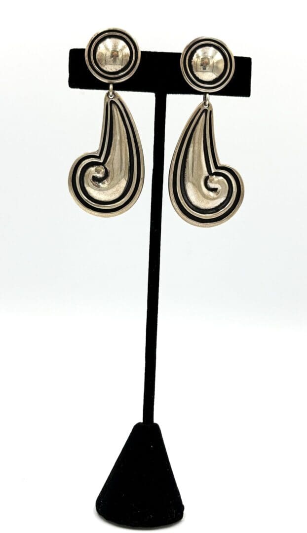 Silver swirl earrings on black stand.