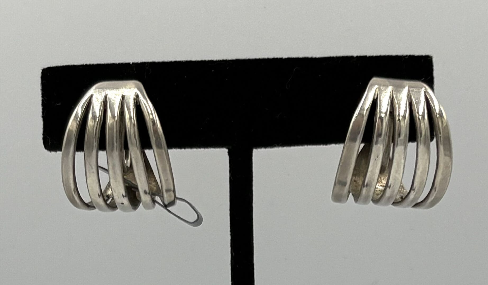 Silver multi-bar earrings on black stand.