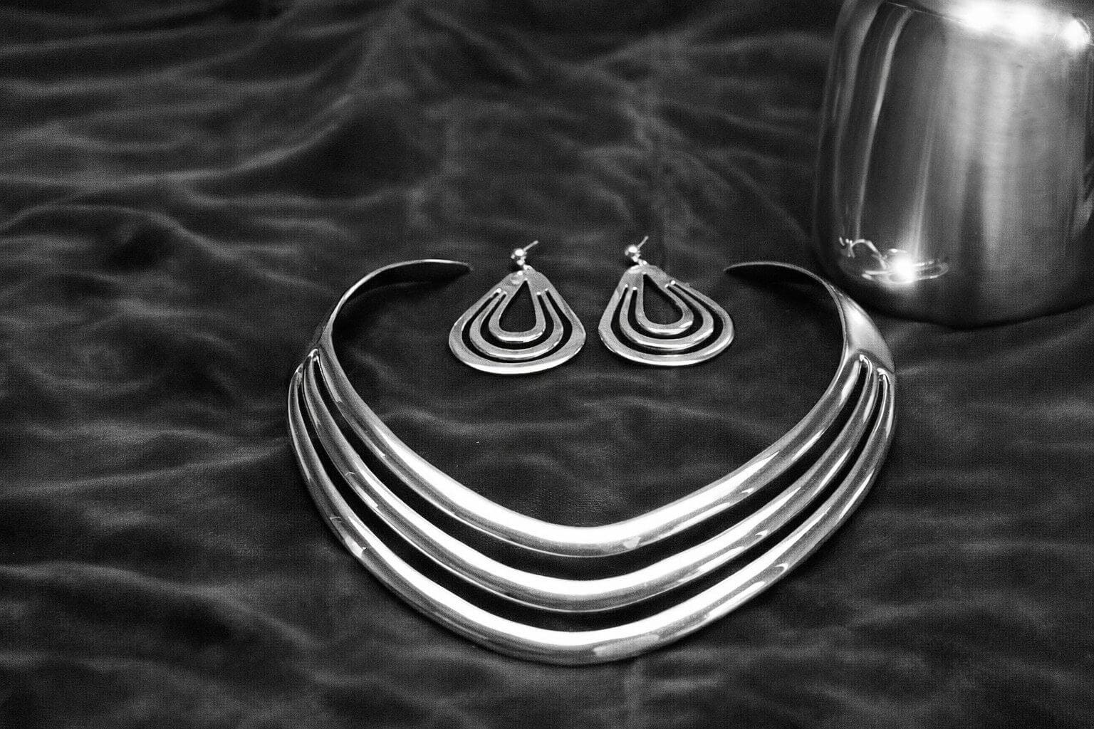 Silver necklace and earrings on dark fabric.