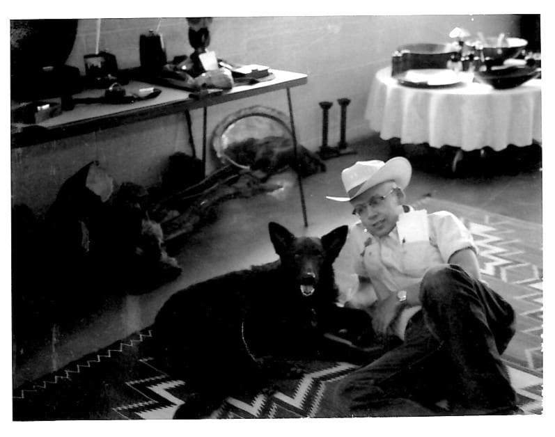 Man in cowboy hat with dog indoors.
