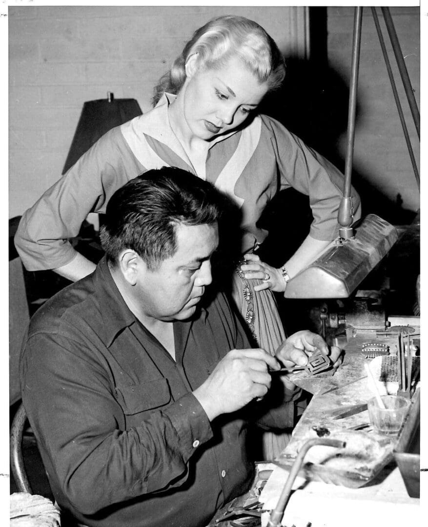 Man crafting jewelry, woman observing attentively.
