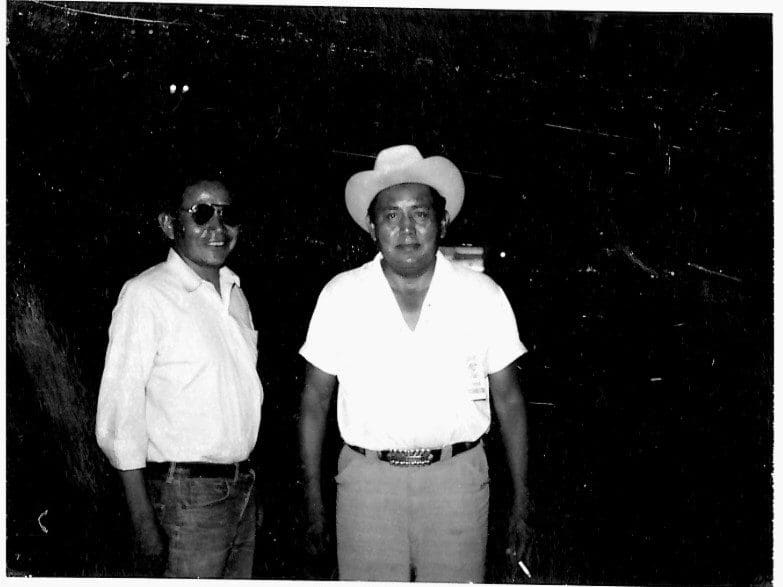 Two men posing, one wearing a hat.