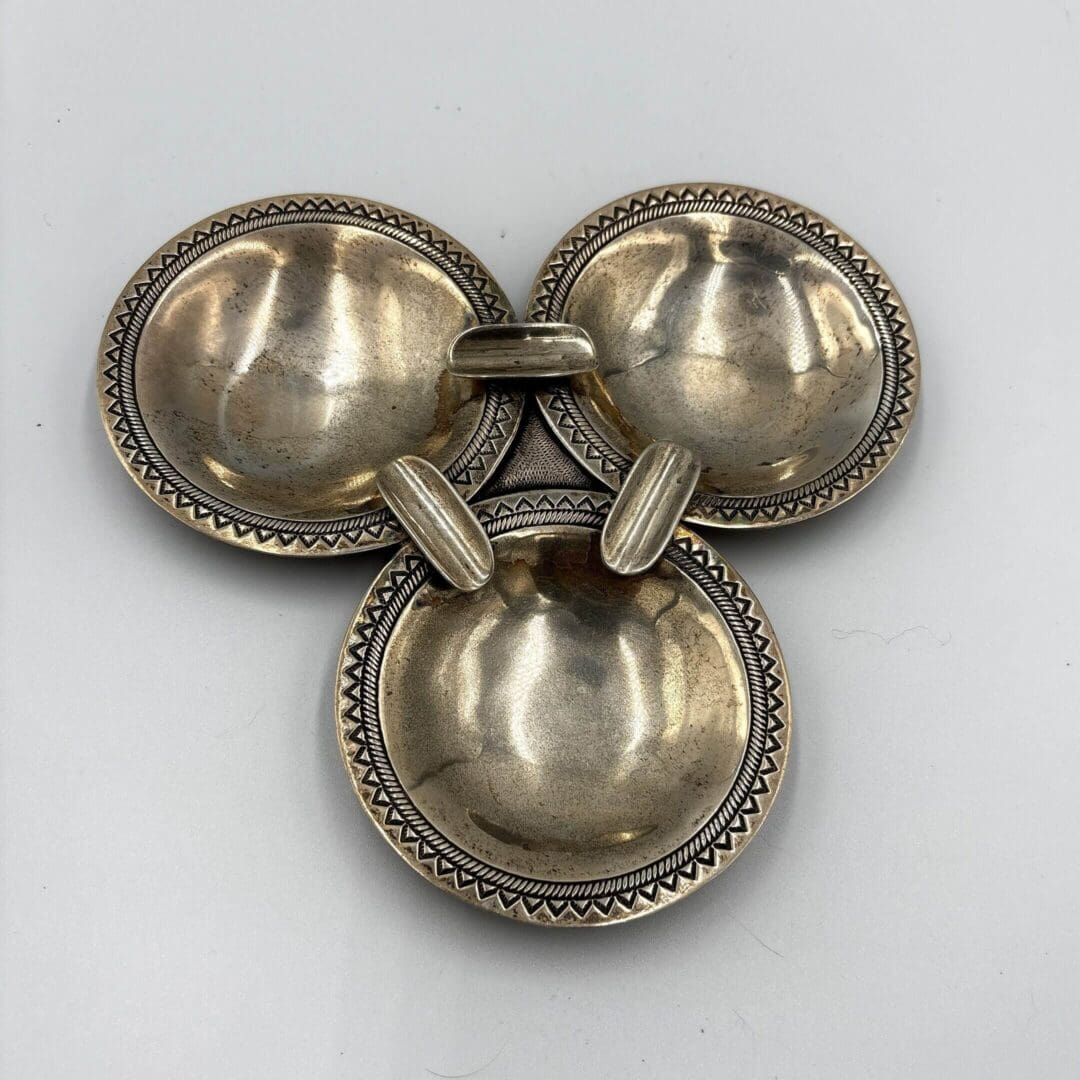 Three connected silver bowls with ornate edges.